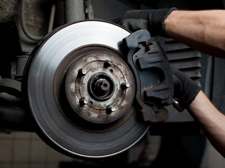 Mechanic wearing gloves working on a car's exposed disc brake system, showcasing the rotor, caliper, and wheel hub—perfectly illustrating expert Brake Services.