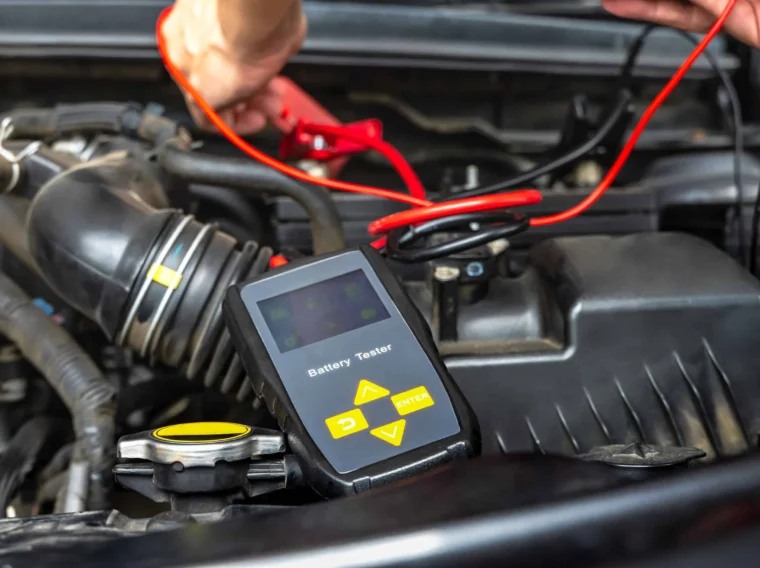 A person uses a battery tester with cables to check a car battery under the hood, demonstrating essential Battery Services.