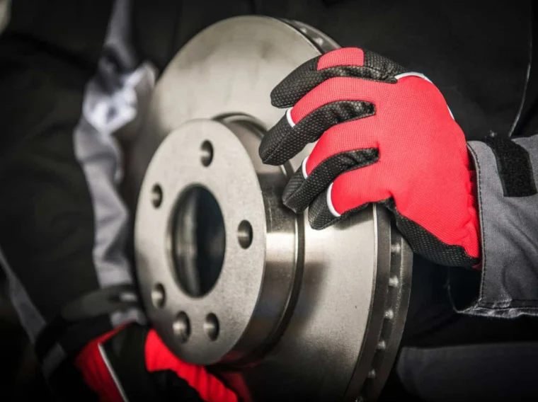 Person wearing red and black gloves holding a metallic automotive brake disc rotor, showcasing the importance of quality Brake Services.