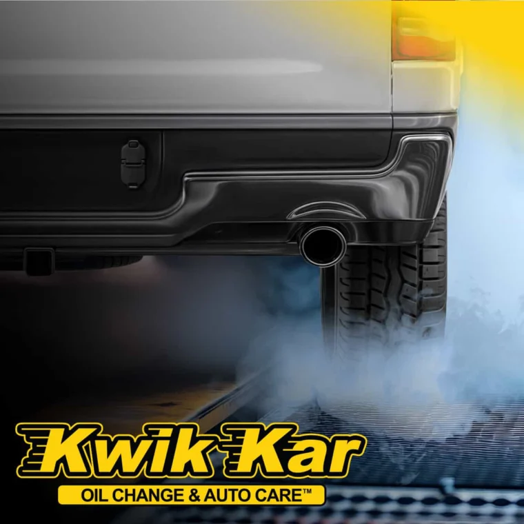 Close-up of a car’s rear bumper and tire with exhaust fumes, overlaid with the Kwik Kar Oil Change & Auto Care™ logo in yellow and black at the bottom.
