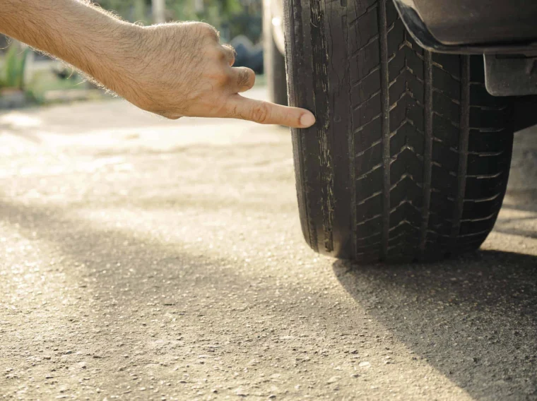 A hand points at a worn car tire with visible tread wear, highlighting the need for replacement or maintenance through professional Tire Services.