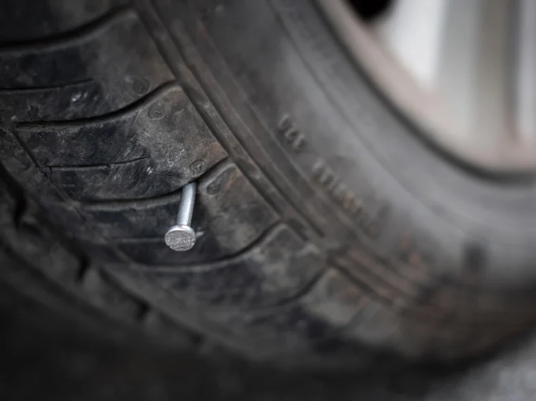 Close-up of a car tire with a nail lodged in the tread, highlighting the need for prompt Tire Services to prevent a flat or air leak.
