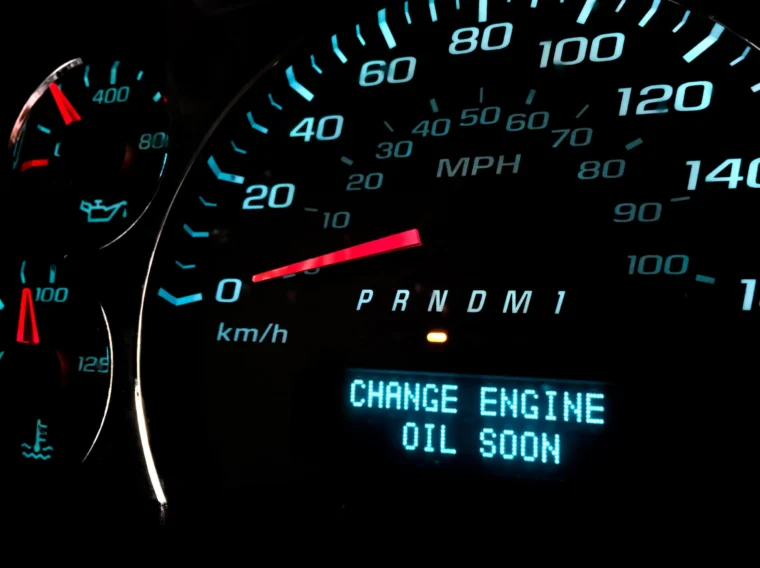 Close-up of a car dashboard showing speedometer, fuel and temperature gauges, and a digital message reading "CHANGE ENGINE OIL SOON.