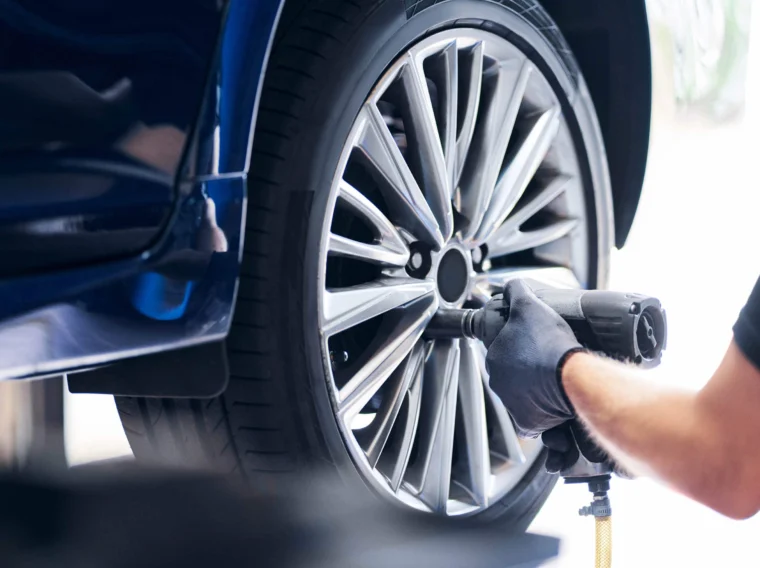 A mechanic wearing gloves uses a power tool to remove or tighten the lug nuts on a car's wheel during a tire replacement.