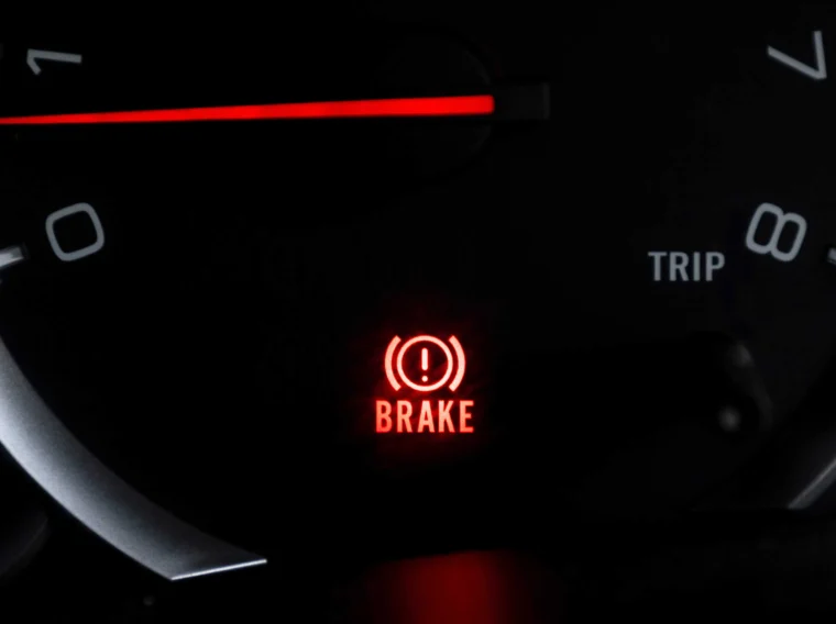 Close-up of a car dashboard with a red brake warning light illuminated and the word "BRAKE" displayed below a symbol.