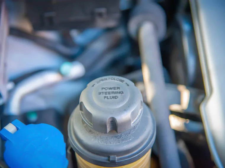 Close-up view of a Power Steering fluid reservoir cap in a car engine compartment, clearly labeled "POWER STEERING FLUID.