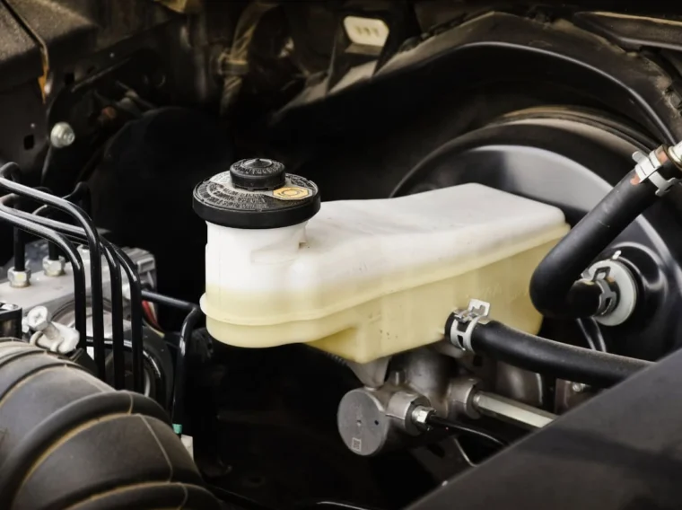 Close-up view of a car's brake master cylinder and reservoir, showing connected hoses and engine components under the hood—ideal for showcasing Fluid Exchange Services in automotive maintenance.