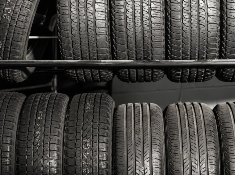 Several rows of new car tires are stacked vertically on metal racks in a store, ready for Tire Replacement and other Tire Services.