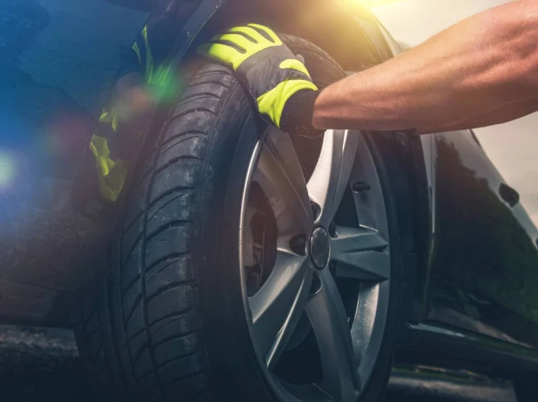 A person wearing yellow gloves is gripping the front tire of a car, possibly checking or changing it as part of routine tire services.