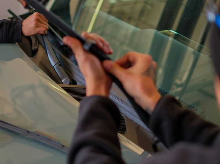 Two people are installing or replacing windshield wiper blades on a car as part of routine maintenance and State Inspection Services.