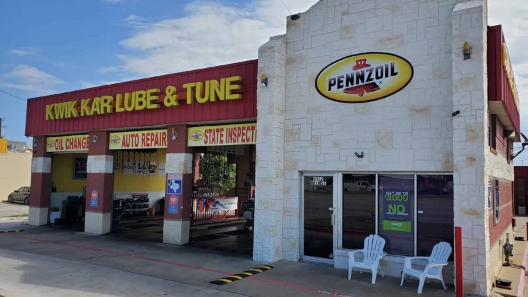 A Kwik Kar Lube & Tune auto repair shop with a Pennzoil sign, open garage bays, and two white chairs outside the office entrance.