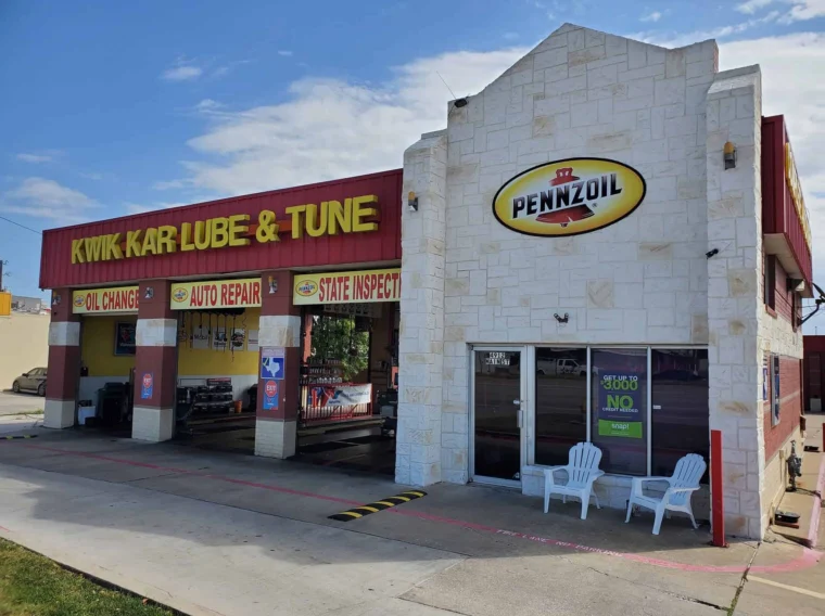 A Kwik Kar Lube & Tune auto repair shop with a Pennzoil sign, open garage bays, and two white chairs outside the office entrance.