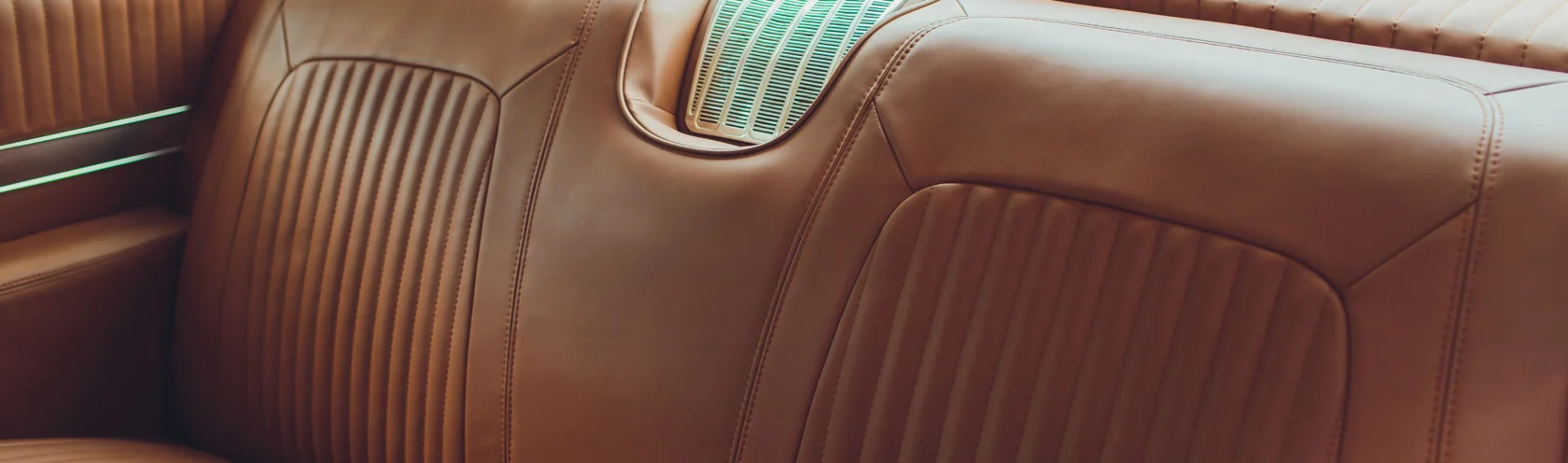 Brown leather backseat of a classic car with vertical stitching and a rear vent grille on the seatback—a true example of Cars of Character.