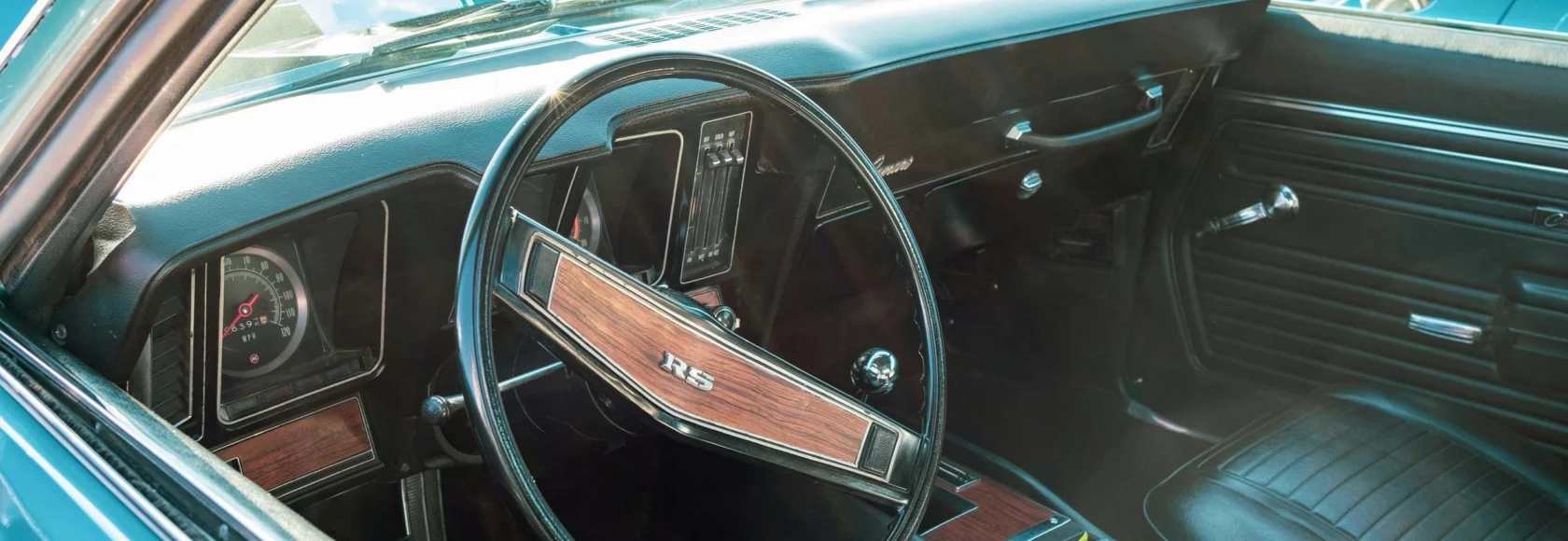 Interior view of a vintage Chevrolet Camaro RS, a true Cars of Character classic, showcasing the steering wheel, dashboard, gear shift, and sleek black leather seats.