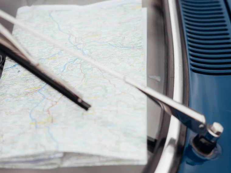 A folded paper map is held under the windshield wiper of a blue car.