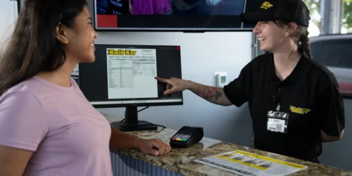 A Kwik Kar employee points at a computer screen while assisting a smiling customer at the service counter.