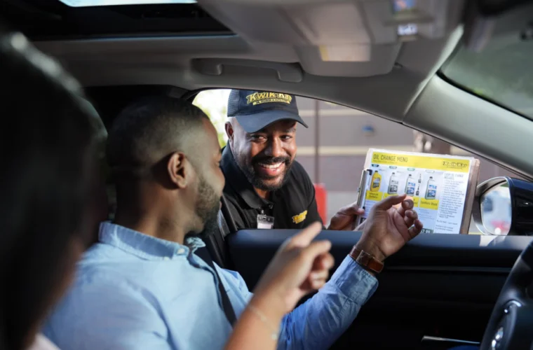 A drive-thru worker hands a menu to two people sitting in a car, as they look at the menu and prepare to order.
